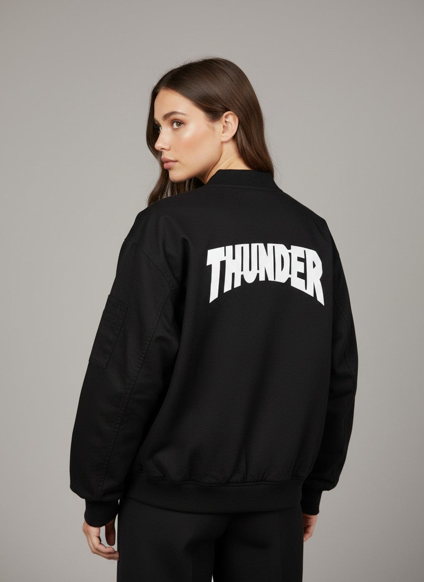 Черно яке тип „бомбър“ от Benny Boutique с бял надпис „THUNDER“ на гърба, показано на жена.