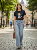 Benny Boutique черна памучна тениска с графичен принт и надпис, носена от жена със светлосини дънки.