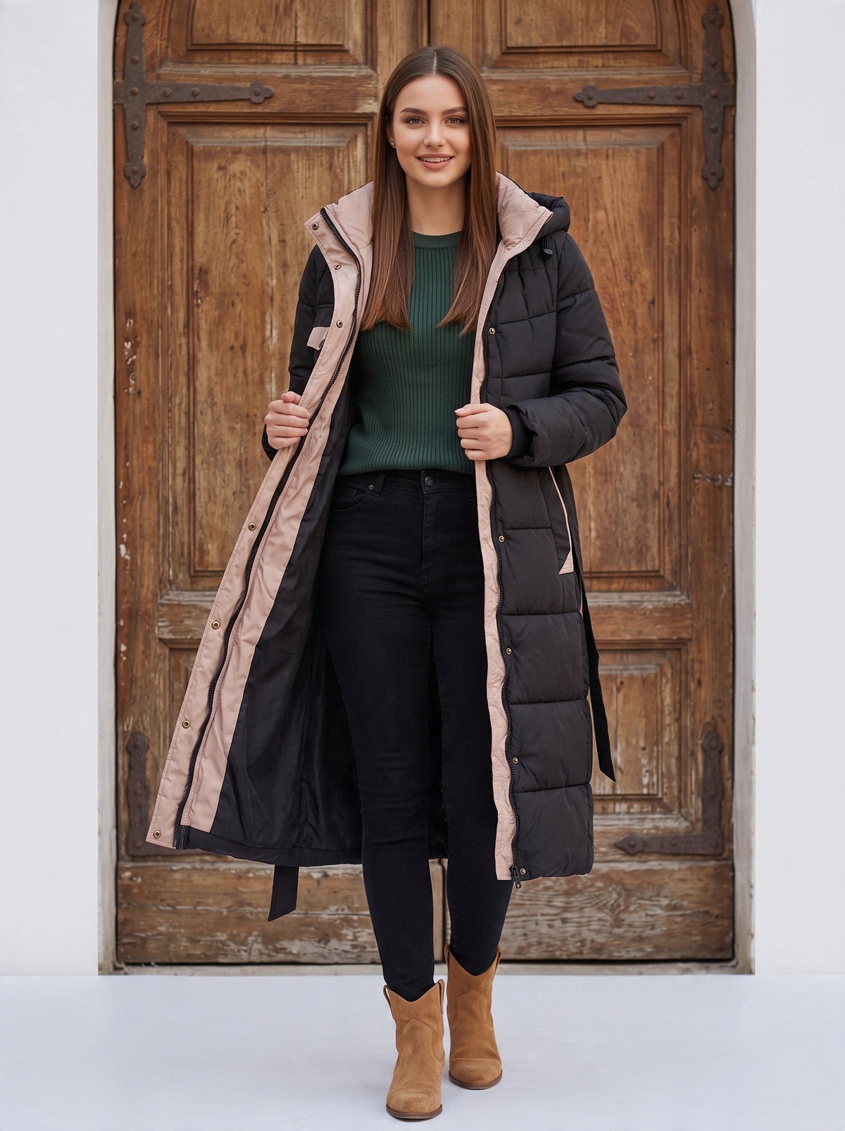 Дълго черно капитонирано пухено палто Benny Boutique с бежови акценти, качулка и колан на талията, облечено от усмихната жена.