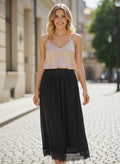 Benny Boutique черна макси пола с дантелено подгъвче, комбинирана с бежова камизола, носена от усмихната жена на градска улица.