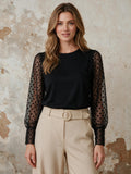 Черна блуза Benny Boutique с прозрачни ръкави от тюл на точки, облечена от моделка с бежов панталон.