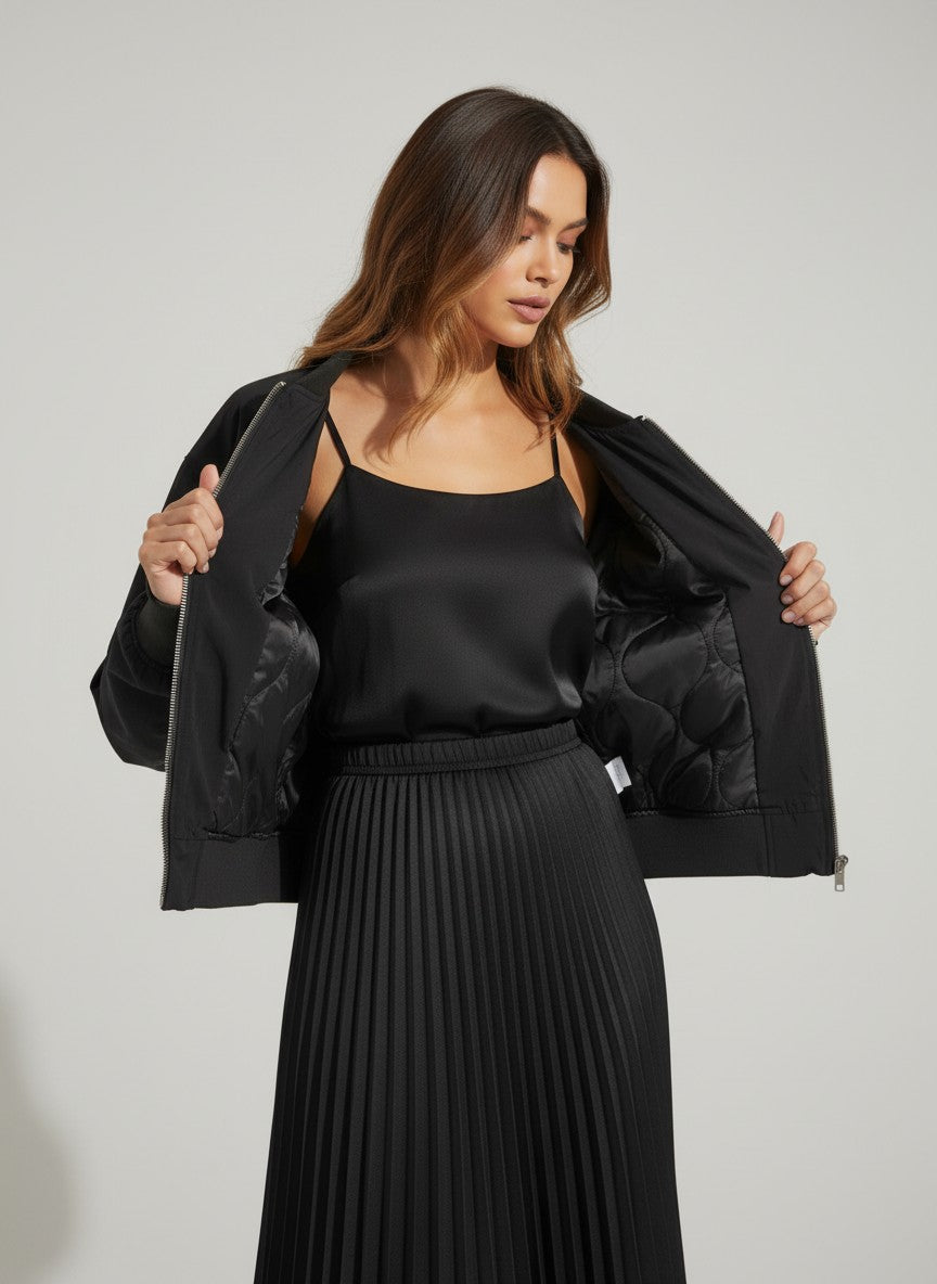 Черно капитонирано яке тип „бомбър“ от Benny Boutique със закопчаване с цип, носено върху подходящ сатенен топ с тънки презрамки и плисирана пола.