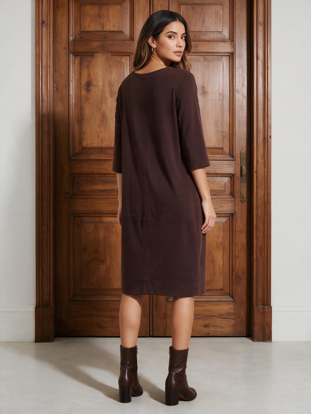 Кафява рокля Benny Boutique с ниска талия и ръкави три четвърти, облечена от жена, застанала пред дървена врата.