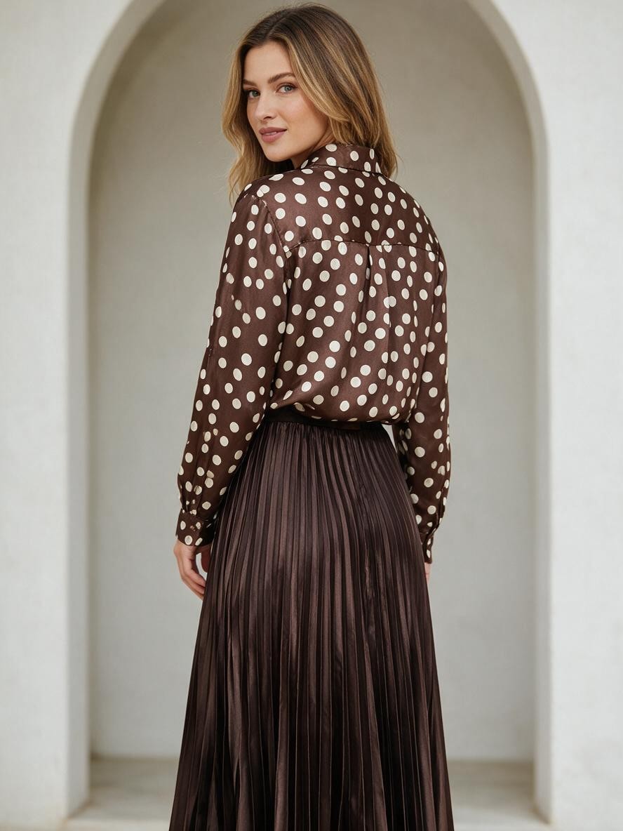 Дълга плисирана пола Benny Boutique в тъмнокафяв цвят, съчетана с подходяща блуза на точки, облечена от русокос модел.