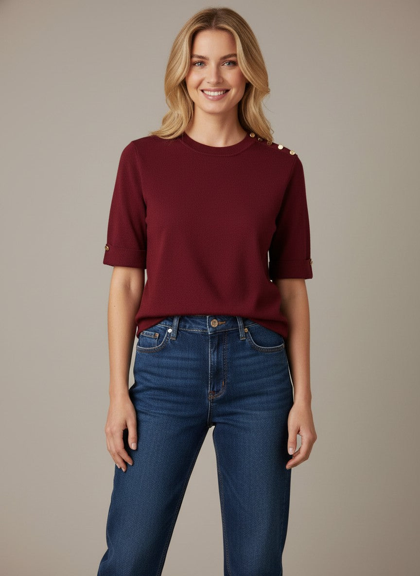Дамска бордо блуза от фино плетиво на Benny Boutique, със златисти копчета на раменете и оребрена обло деколте, съчетана със сини дънки.
