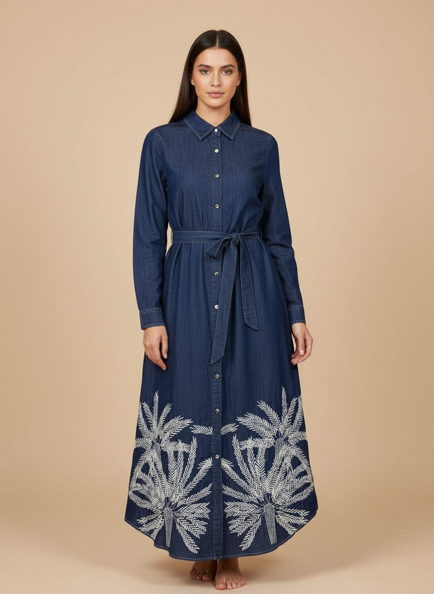 Макси рокля от тъмен син деним на Benny Boutique с бели бродирани мотиви на палмови листа и колан за подчертаване на талията.
