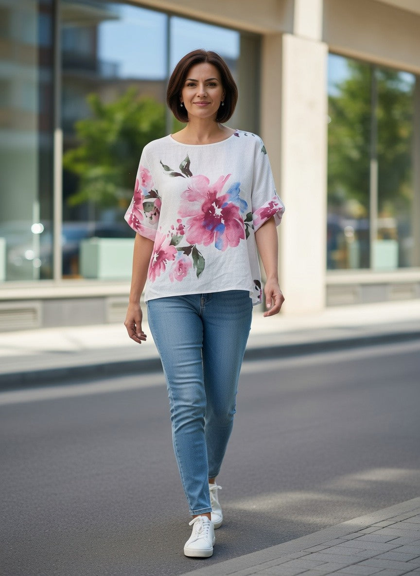 Benny Boutique свободна бяла блуза с розово-син флорален принт, носена от жена с дънки на градска улица.