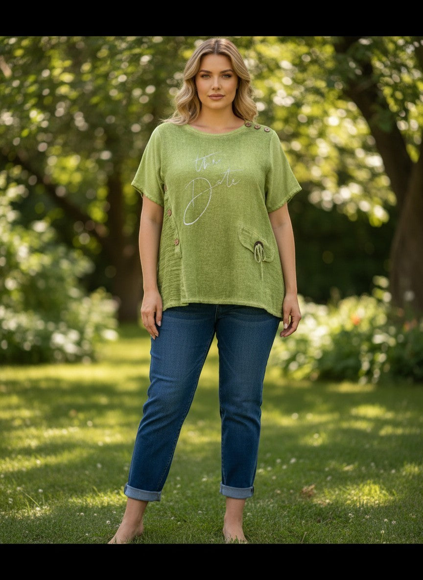 Зелена макси А-образна блуза на Benny Boutique с асиметрични копчета и бял текст, носена от жена в парк.