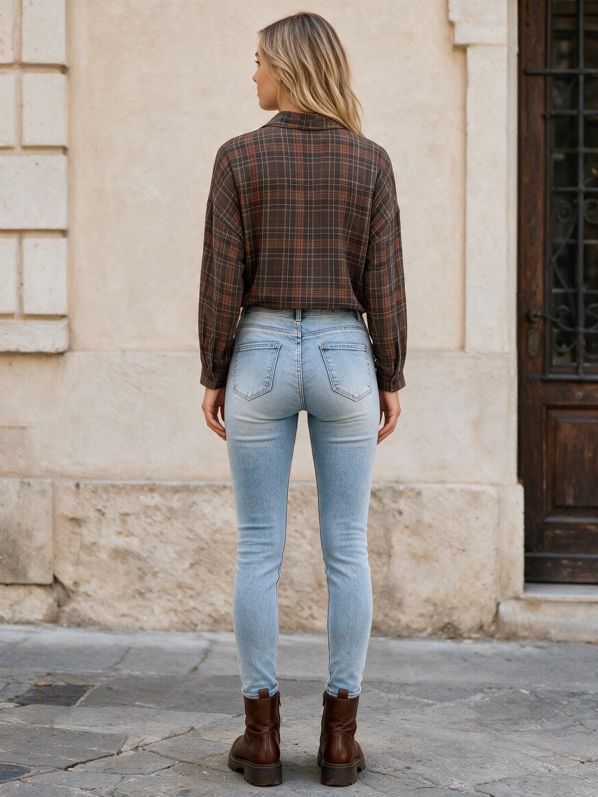 Светлосини тесни дънки Benny Boutique с избелял ефект, съчетани с карирана риза и кафяви боти, облечени от жена.