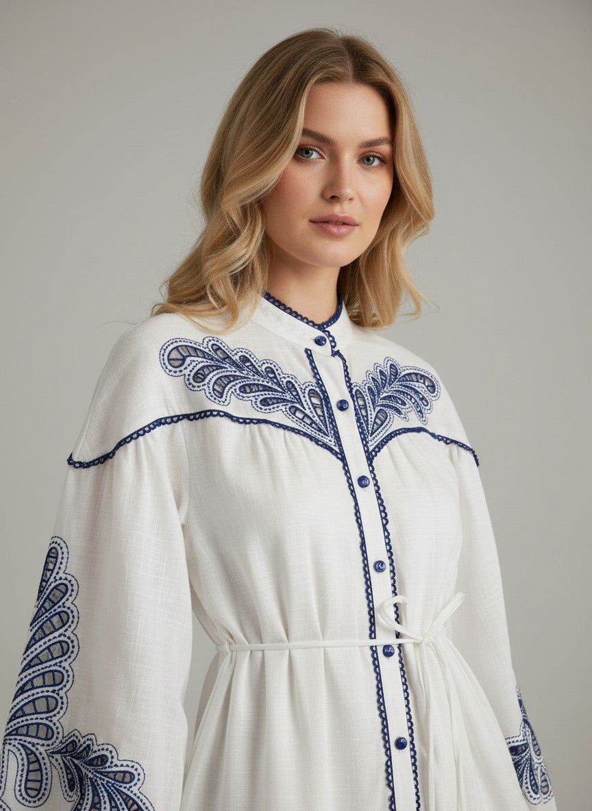 Бяла миди рокля Benny Boutique с детайлна синя бродерия на гърдите и ръкавите, с предно закопчаване с копчета.