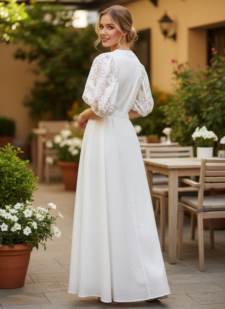 Бяла макси рокля Benny Boutique с бродирани буфан ръкави и романтичен разкроен силует, представена в градинска обстановка.