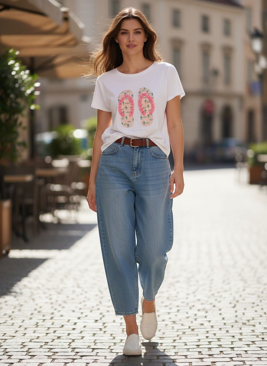 Benny Boutique бяла памучна тениска с розов принт на джапанки и релефни детайли. Моделът я носи със светли дънки.