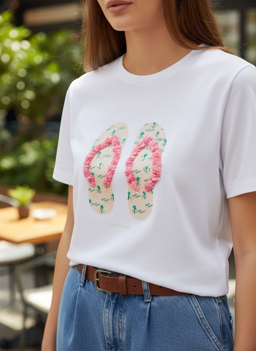 Benny Boutique бяла памучна тениска с розов принт на джапанки и релефни детайли. Моделът я носи със светли дънки.