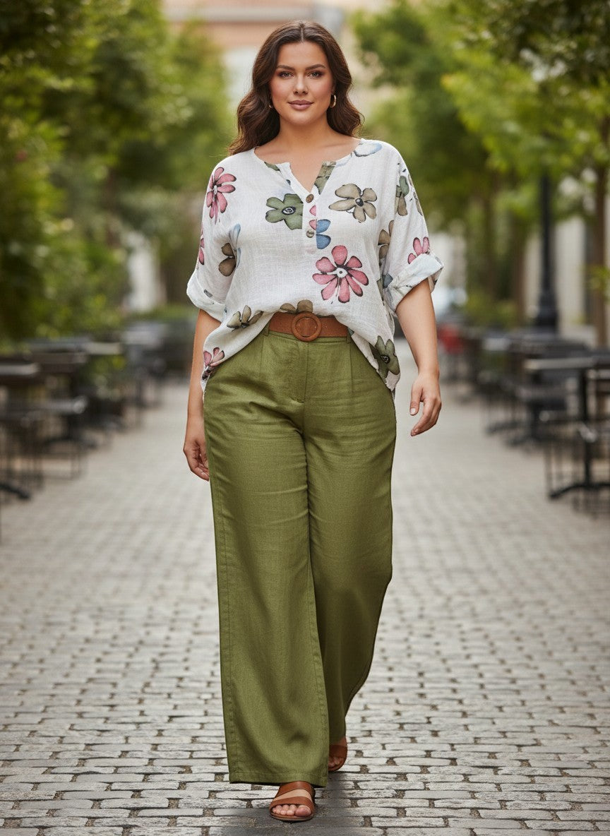 Бяла флорална блуза на Benny Boutique с ретро принт, носена от модел с маслинено зелени широки панталони на градска улица.
