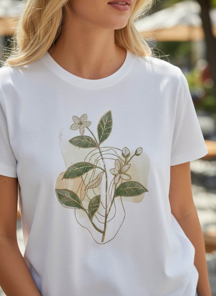 Бяла памучна тениска на Benny Boutique със зелен флорален принт и фини златисти акценти, носена от руса жена.