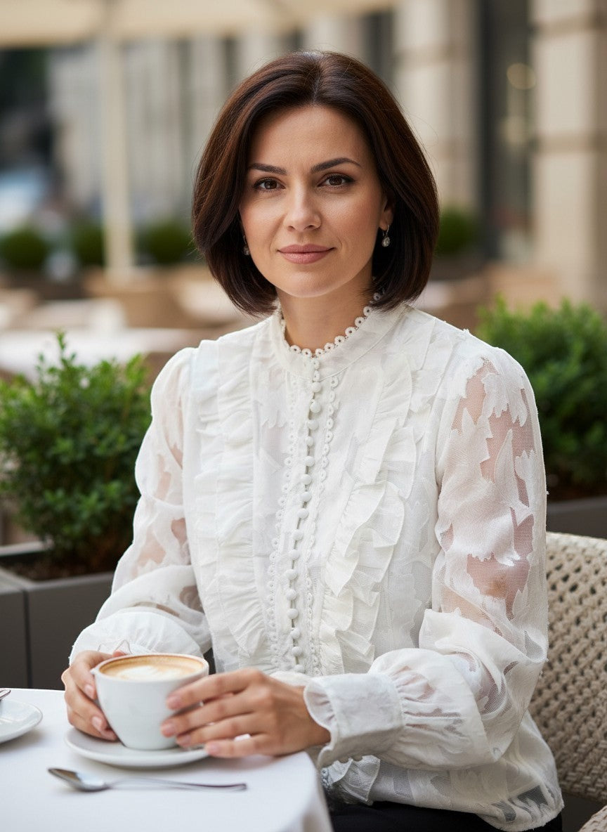 Benny Boutique бяла прозрачна блуза с флорален релеф, къдри и предно закопчаване с копчета, носена от жена в кафене.