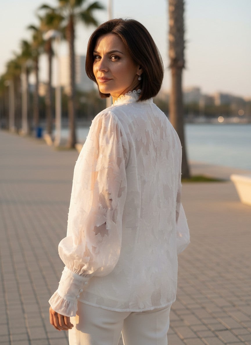 Benny Boutique бяла прозрачна блуза с флорален релеф, къдри на маншетите и висока яка, носена от жена на открито.